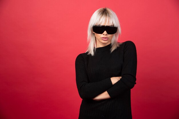 Portrait of woman standing and posing with a black glasses on a red wall.