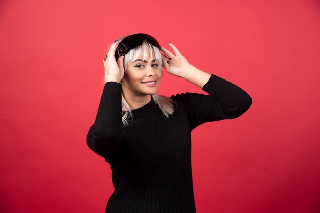 Portrait of woman standing and posing with a black glasses on a red wall.