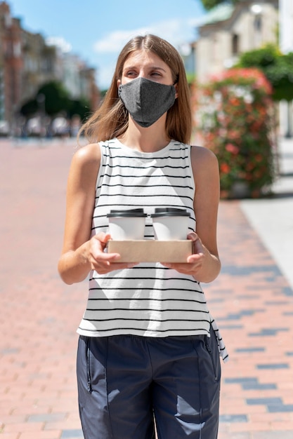 Foto gratuita donna del ritratto sulla via con la maschera da portare del caffè