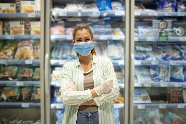 Free photo portrait of woman in supermarket with protection mask and gloves standing by the food in grocery store