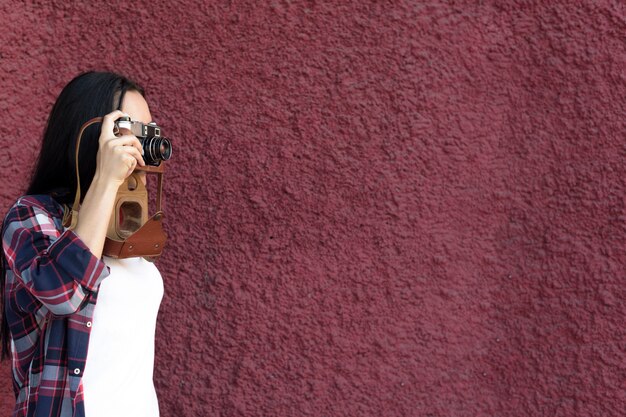 Portrait of woman taking photograph with camera against maroon textured wall