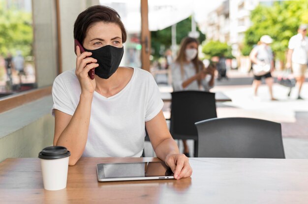 Free photo portrait woman at terrace with tablet wearing mask