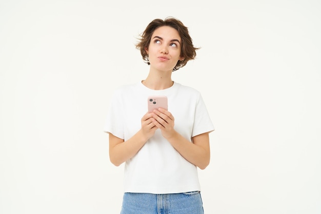 Free photo portrait of woman thinking using smartphone and looking thoughtful making choice deciding standing