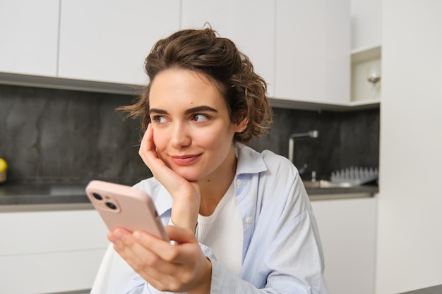 Free photo portrait of woman thinking while holding smartphone deciding what to order on mobile phone app