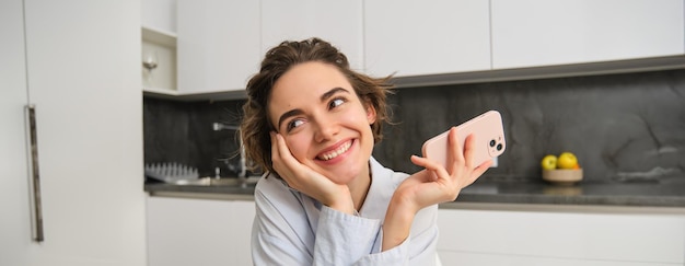 Free photo portrait of woman thinking while holding smartphone deciding what to order on mobile phone app