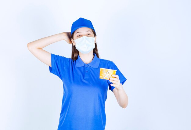 プラスチック製のコップを保持している制服と医療マスクの女性の肖像画