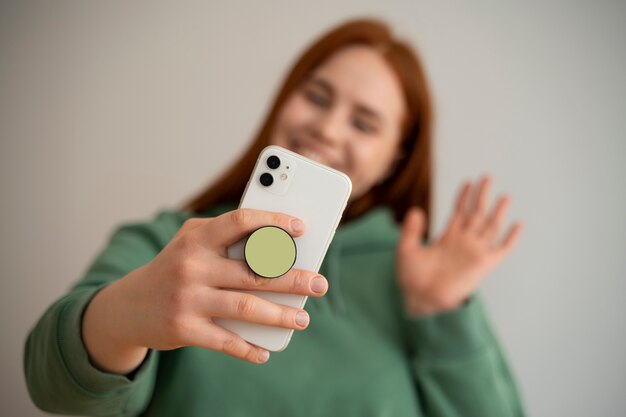 ポップ ソケットから保持して自宅のソファで彼女のスマート フォンを使用している女性の肖像画