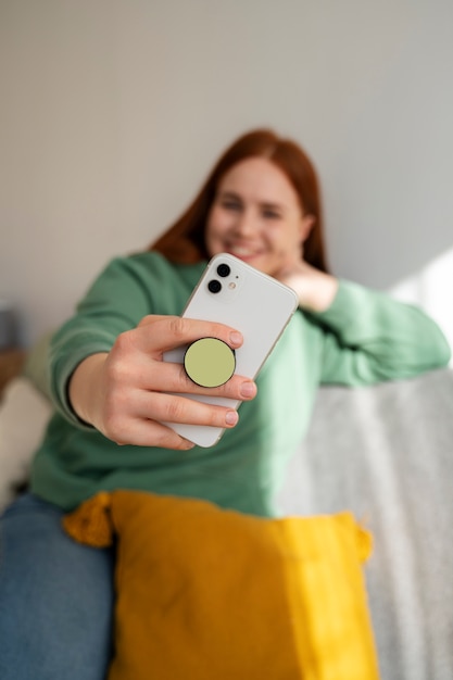 Portrait of woman using her smartphone at home on couch by holding from pop socket