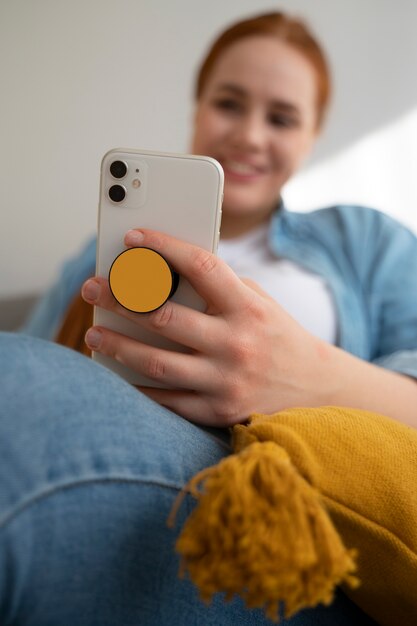 ポップ ソケットから保持して自宅のソファで彼女のスマート フォンを使用している女性の肖像画