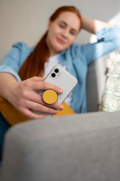 Portrait of woman using her smartphone at home on couch by holding from pop socket