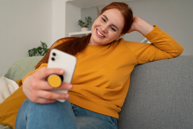 Portrait of woman using her smartphone at home on couch by holding from pop socket