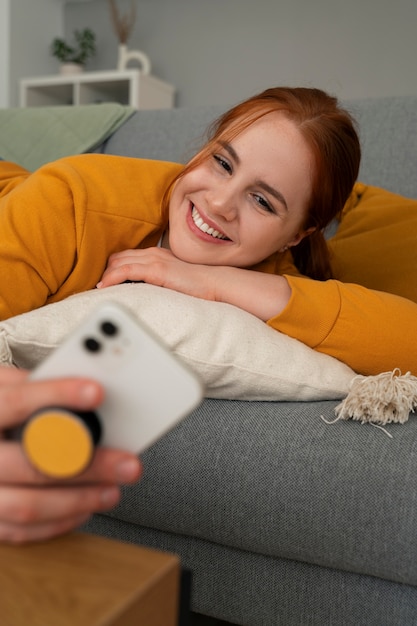 Free photo portrait of woman using her smartphone at home on couch by holding from pop socket