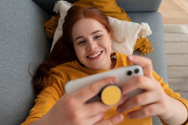 Portrait of woman using her smartphone at home on couch by holding from pop socket