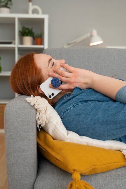 Free photo portrait of woman using her smartphone at home on couch by holding from pop socket