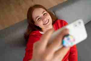 Free photo portrait of woman using her smartphone at home on couch by holding from pop socket