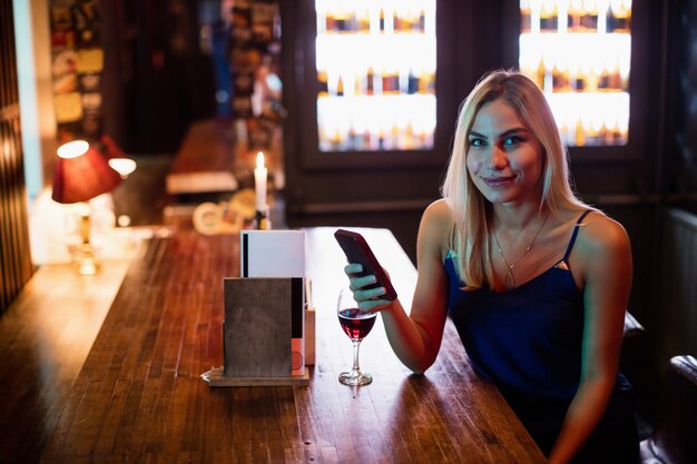 Portrait of woman using mobile phone with red wine on table