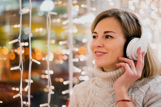 Portrait of woman wearing headphones near christmas lights