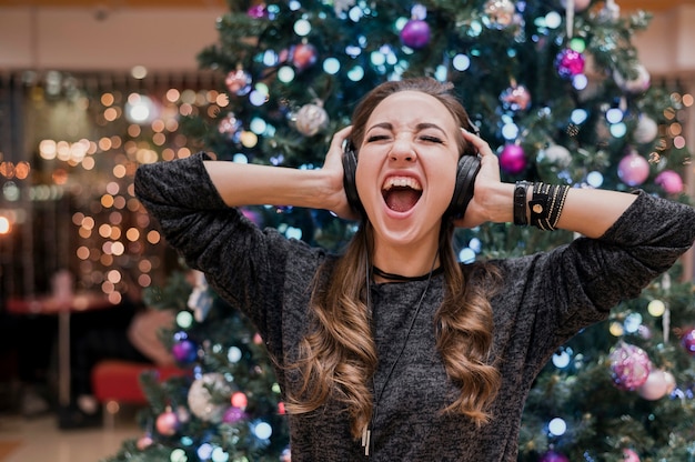 Portrait of woman wearing headphones and shouting near christmas tree