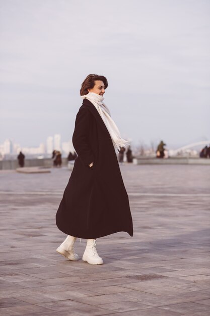 Portrait of woman in winter black coat and white scarf on city square.