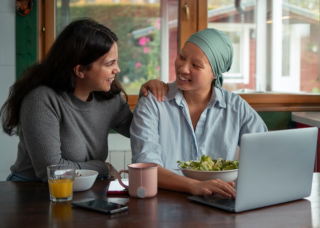 Portrait of woman with cancer using laptop with friend at home