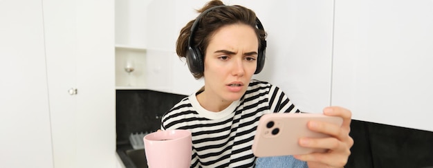 Free photo portrait of woman with confused face wearing headphones watching tv series or show on smartphone app