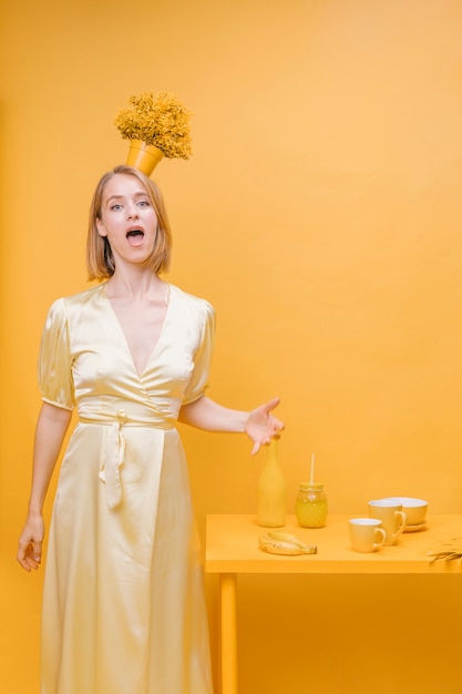 Free photo portrait of woman with flower pot on head in a yellow scene