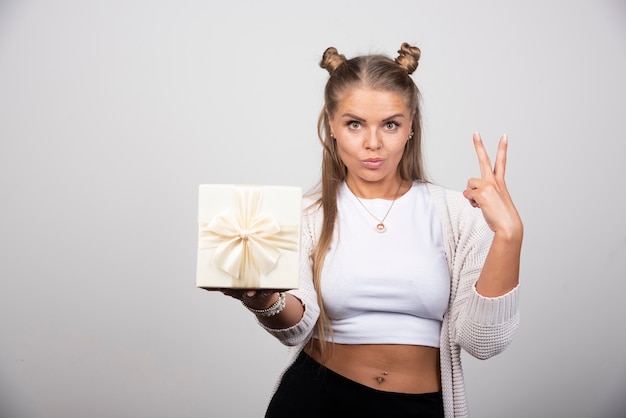 Portrait of woman with gift box giving victory sign.