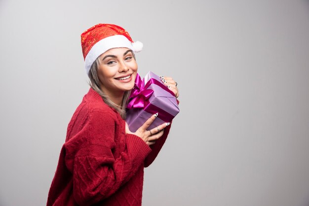 Portrait of woman with gift box smiling on gray background.