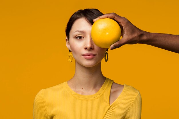 Portrait of woman with grapefruit held by man covering her eye