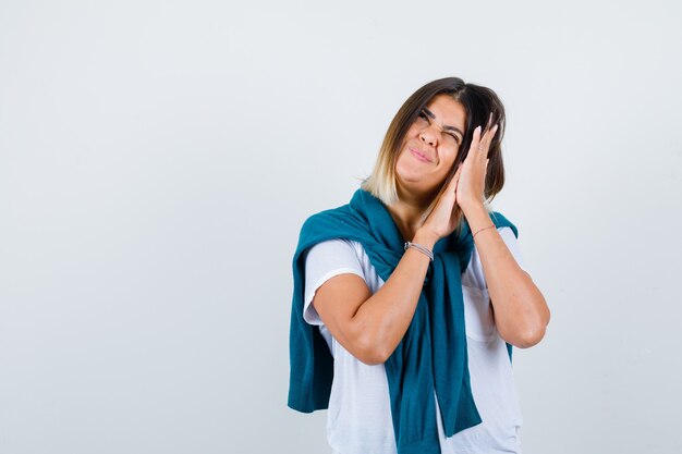 Portrait of woman with tied sweater leaning on palms as pillow in white t-shirt and looking positive front view