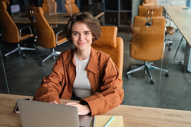 Ritratto di donna che lavora in ufficio seduto al tavolo con un programmatore di una ragazza portatile che codifica in coworking