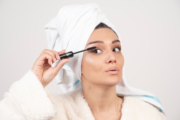 Portrait of woman wrapped in white towel applying mascara .