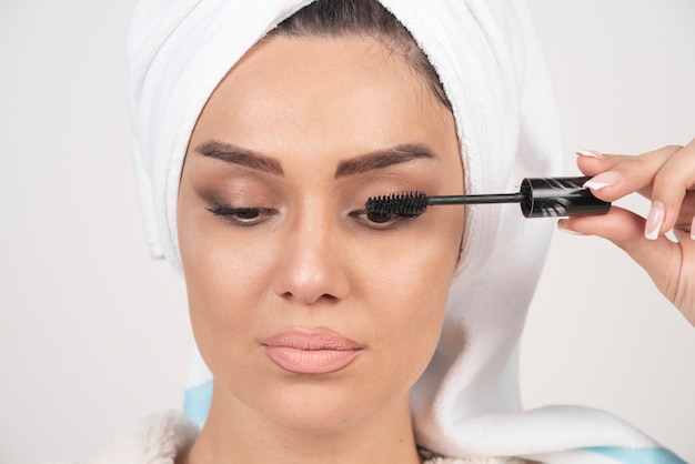 Free photo portrait of woman wrapped in white towel applying mascara