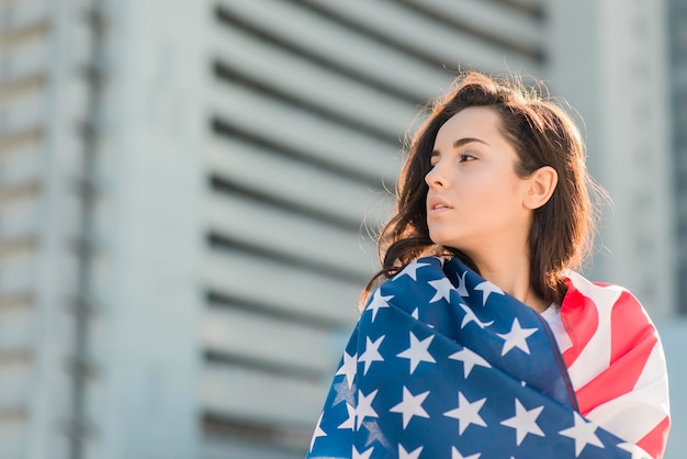 Free photo portrait of woman wrapping herself in usa flag looking away