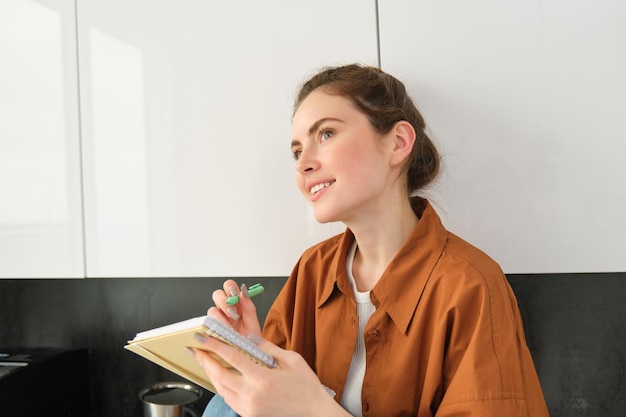 Portrait of woman writing down her ideas in a notebook holding pen and looking thoughtful inspired