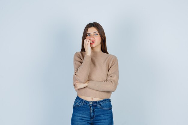 Портрет прекрасной дамы, кусающей ногти в свитере, джинсах и обеспокоенной взглядом спереди
