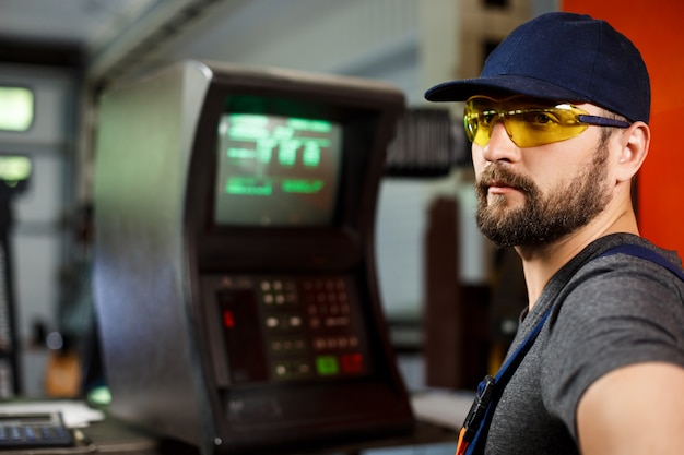 Portrait of worker in onalls near computer, steel factory background.