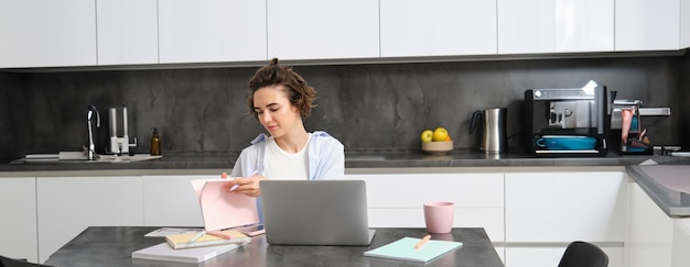 Free photo portrait of working woman at home checks her notebook flips page connects to online meeting via