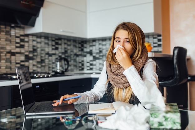 Ritratto di una donna d'affari preoccupata che tiene in mano i tovaglioli e starnutisce a casa in cucina e usa il laptop