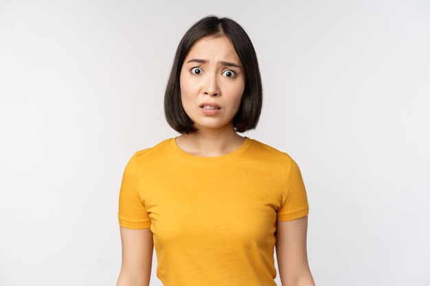 白い背景の上に黄色のTシャツに立っているカメラを心配している韓国の女の子の肖像画