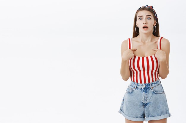 Portrait of worried overreacting cute woman in striped top and shorts pointing at herself questioned and nervous being confused and accused