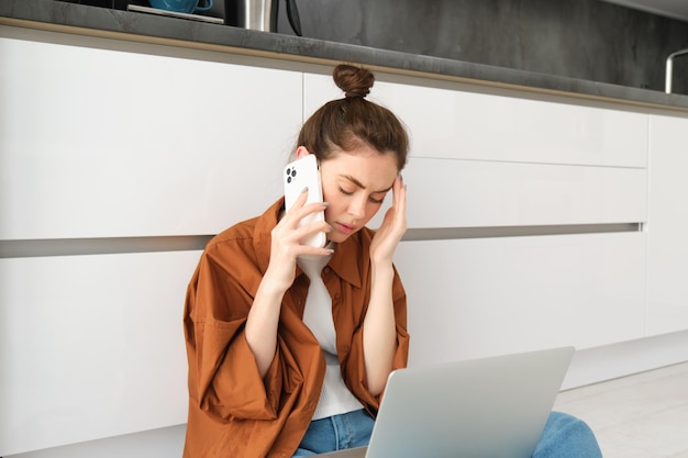 Free photo portrait of worried woman sits on floor with laptop listens to bad news over the phone calling
