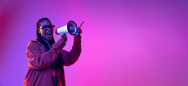 Портрет молодой стильной девушки, кричащей в мегафон, изолированной на градиентном розово-фиолетовом фоне