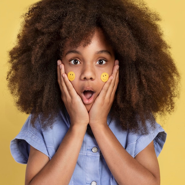 Free photo portrait of young adorable girl posing with emoji stickers on her face