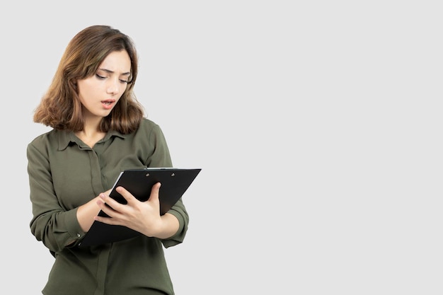 Portrait of young adorable woman reading notes on clipboard. High quality photo