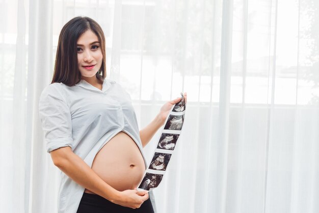 Portrait of young adult asian pregnant woman holding ultrasound scan photo with happy