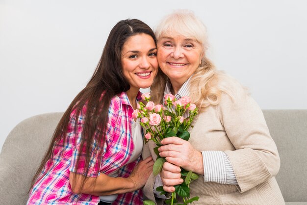 Portrait of young adult woman comforting her senior mother holding rose bouquet