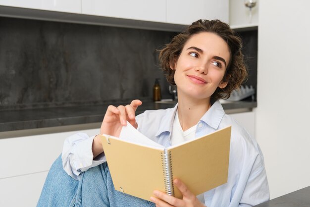 Portrait of young adult woman reading her notes holding notebook and smiling relaxing at home