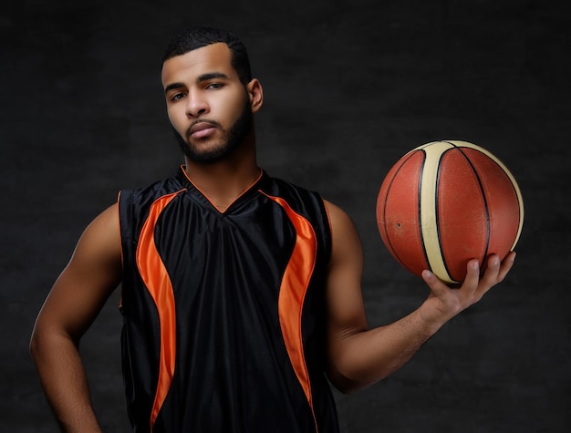 Foto gratuita ritratto di un giovane giocatore di basket afroamericano in abbigliamento sportivo isolato su sfondo scuro.