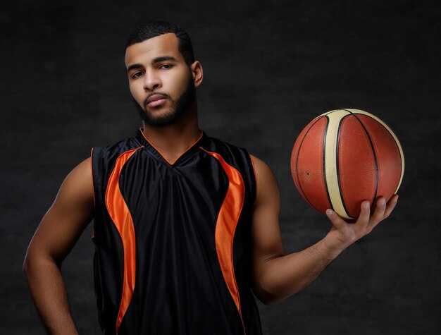 Portrait of a young African-American basketball player in sportswear isolated over dark background.